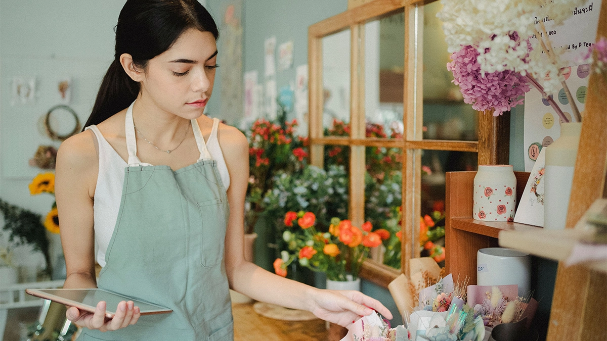 Young female florist owner holding tablet looking at flowers